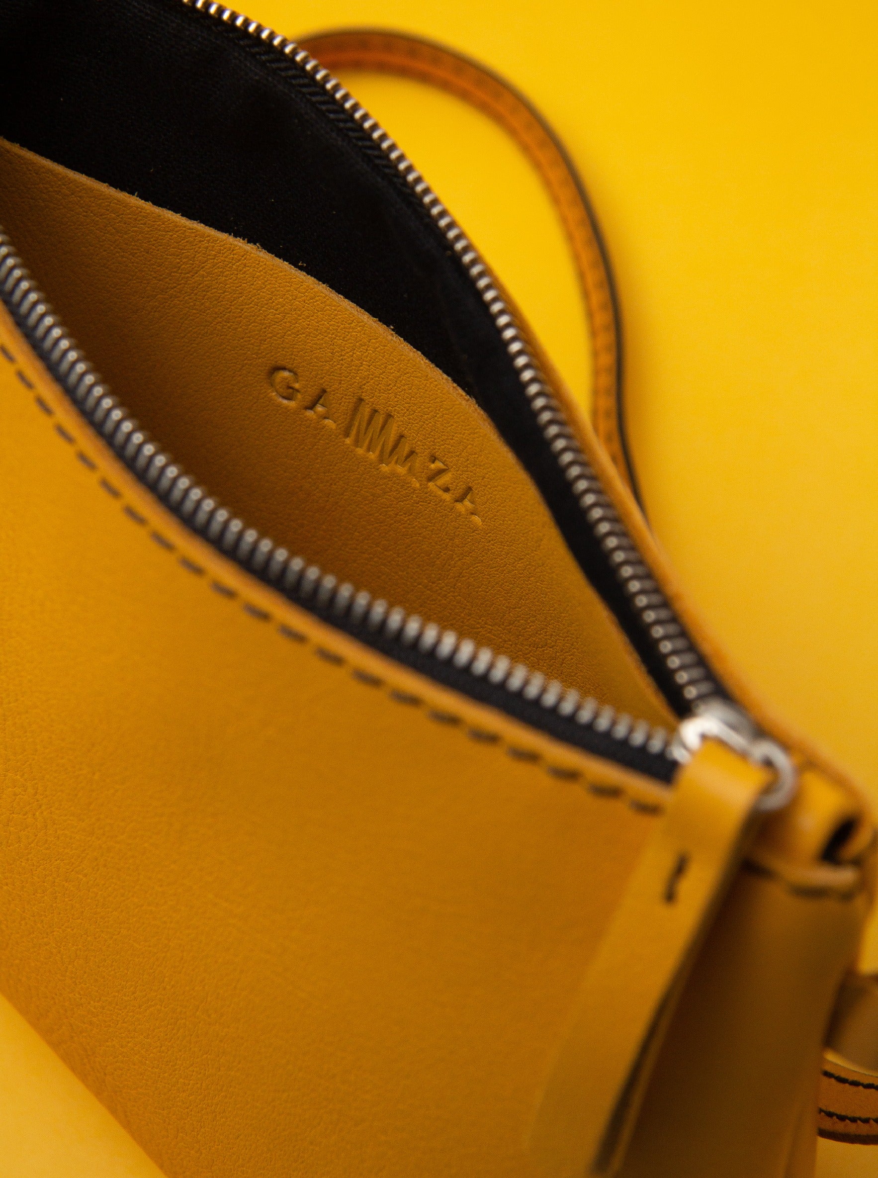 Bolso de cuero amarillo mostaza con cremallera y bolsillo interior.